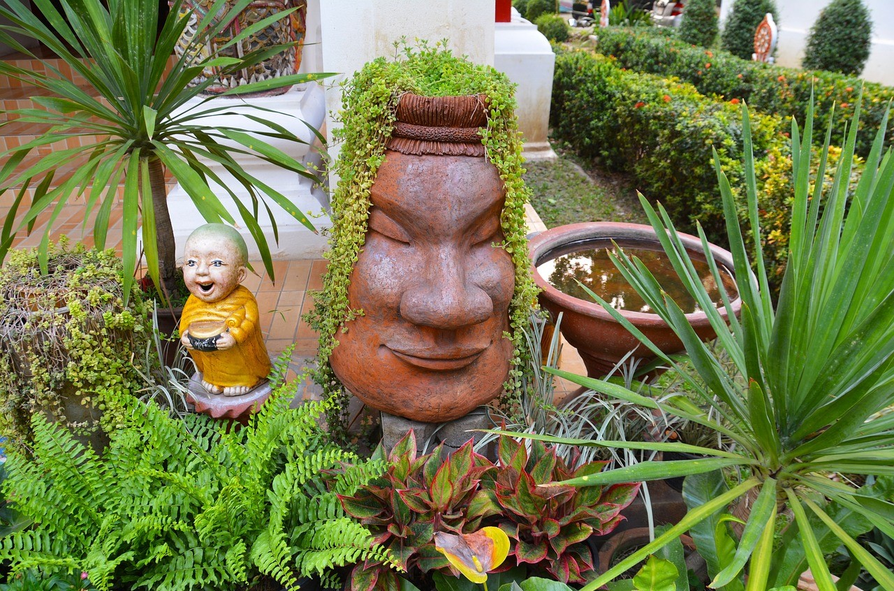 Face statue with greenery growing as hair and a bird bath surrounded by plants